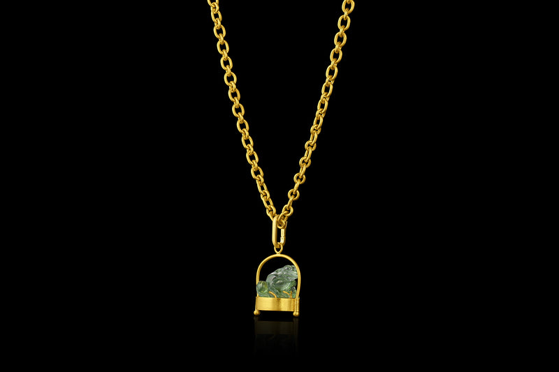 Craved green tourmaline frog pendant on gold base and wire frame. Laying down. On chain. 