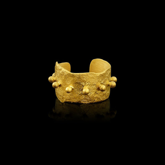An ear cuff formed from a hammered sheet of gold, accented with a spine of gold balls, featuring an organic edge inspired by papyrus, the reed paper used by the ancient Egyptians. 
