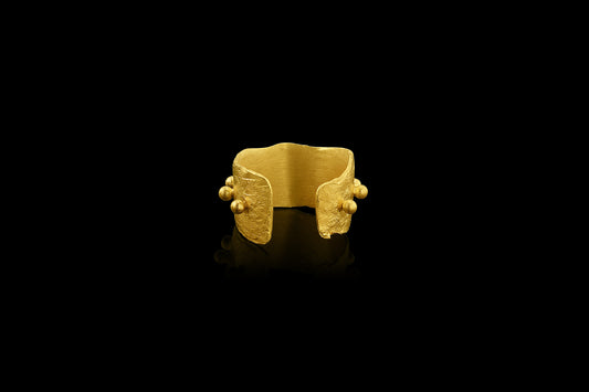 An ear cuff formed from a hammered sheet of gold, accented with a spine of gold balls, featuring an organic edge inspired by papyrus, the reed paper used by the ancient Egyptians. 