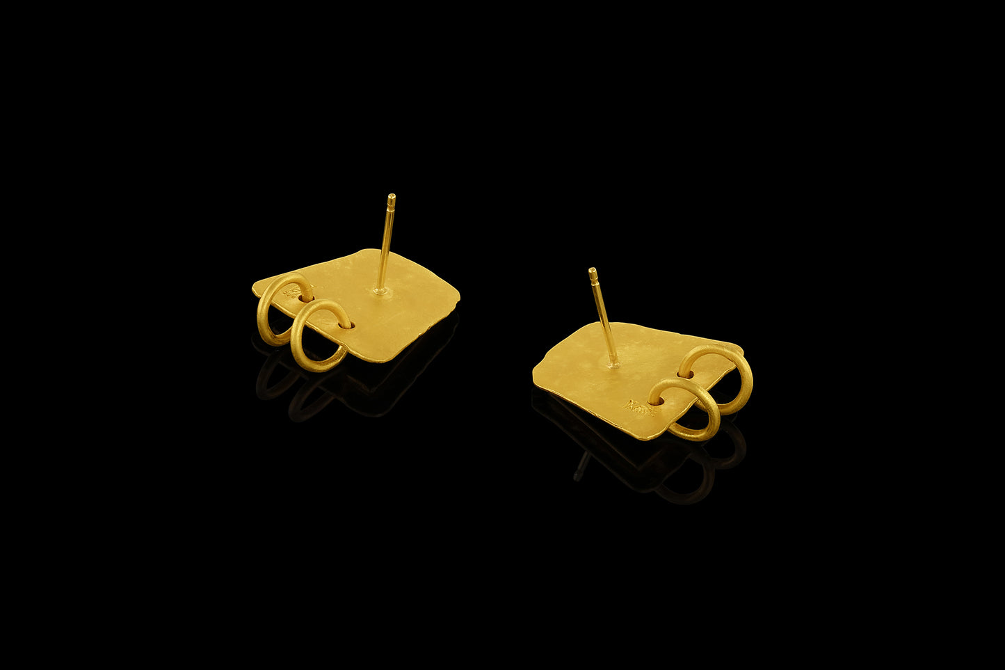 Earrings based on the shape of ancient tablets, featuring a textured surface and suspending two hoops. Back. 