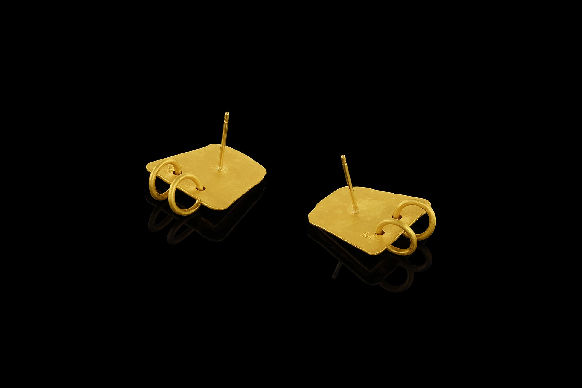 Earrings based on the shape of ancient tablets, featuring a textured surface and suspending two hoops. Back. 